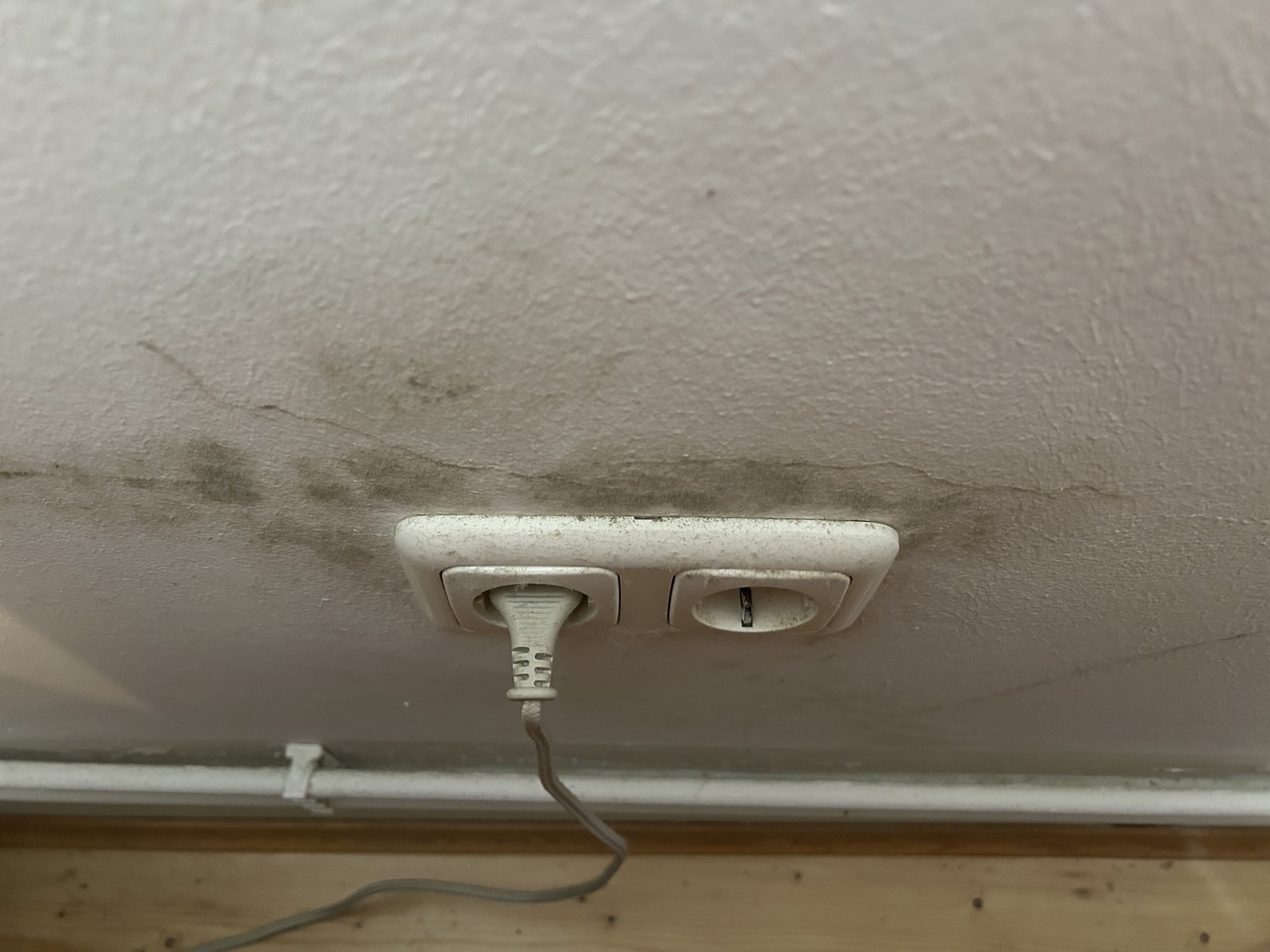 Schwarzer Schimmelbefall rund um eine Steckdose an einer kalten Außenwand hinter einem Schrank